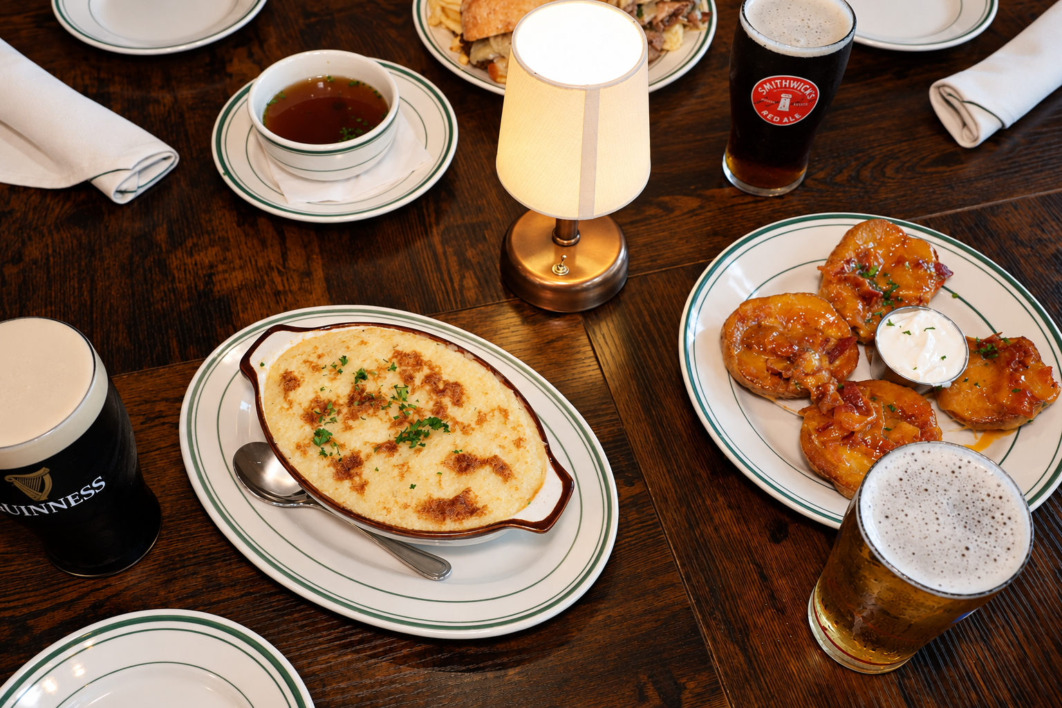 A table spread with shepherd's pie, potato skins, French dip, and pints